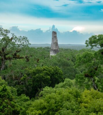 An ancient Mayan monument in Tikal National Park, Guatemala, Central America A scenic view of the Tikal Temple rising above the lush green jungle under a partly cloudy sky in Guatemala.